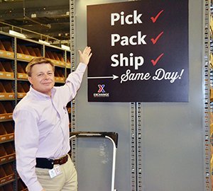 Dave Nelson gestures at "Pick, Pack, Ship - Same Day!" sign