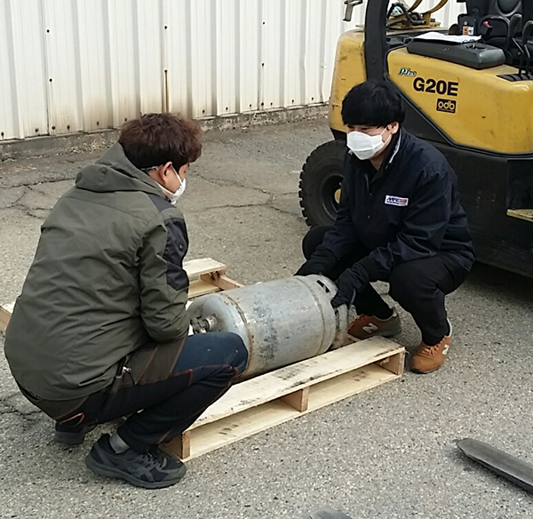 At the Korea Distribution Center, Storage Clerk Song-Hak Chon and MHE operator Yong-Po Sim use the team lift when replacing the forklift's gas tank.