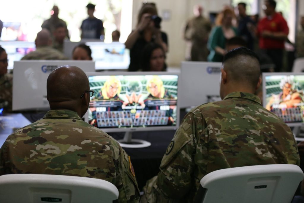 Two Soldiers play a video game on a large screen.