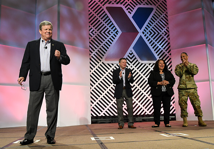 Exchange Director/CEO Tom Shull speaks to the MSM/GM Conference. He is flanked by Chief Operating Officer Dave Nelson, President and Chief Merchandising Officer Ana Middleton, and Senior Enlisted Advisor CMSgt Luis Reyes.