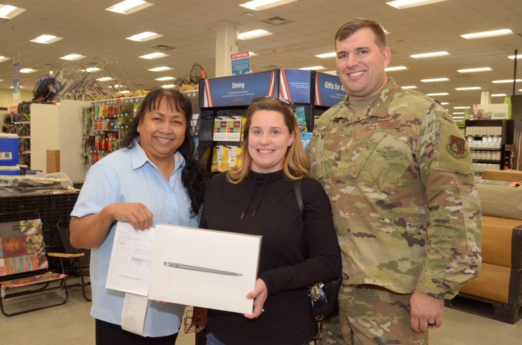 <stromg>Air Force Master Sgt. Brett Myers, Engineering Craftsman with the 718th Civil Engineer Squadron, and his wife, Misti, pose for a picture with Flor Payton, Kadena Exchange main store manager, after Brett surprised Misti with a MacBook Pro. Brett used the Exchange’s layaway program for the first time to purchase the laptop for Misti, who is pursuing a degree in medical administration. On Dec. 15, Brett was invited to a video call with celebrity and Marine and Navy Veteran, Montel Williams. During the call, Williams announced that all Exchange layaways in the Pacific Region, including Brett’s, were paid in full by nonprofit Pay Away the Layaway. (U.S. Army Photo by Staff Sgt. Mark A. Kauffman)</strong>