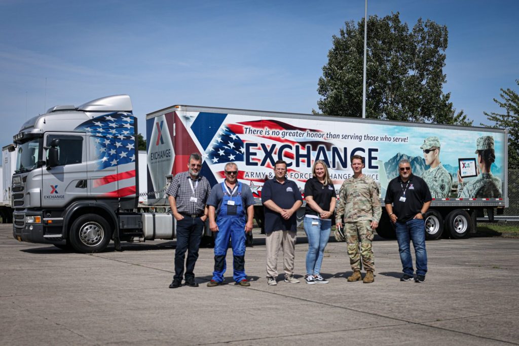 Exchange Europe/Southwest Asia/Africa Commander Col. Bud Lacroix and five Germersheim Distribution Center associates in front of a semi-truck with an Exchange truck wrap featuring the U.S. flag.