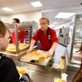 An Exchange school meal program associate serves schoolchildren a tray of food.