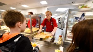 An Exchange school meal program associate serves schoolchildren a tray of food.