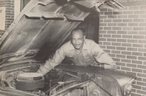 1963 photo of Richard Drew, who has a prosthetic left arm, working under the hood of a car.